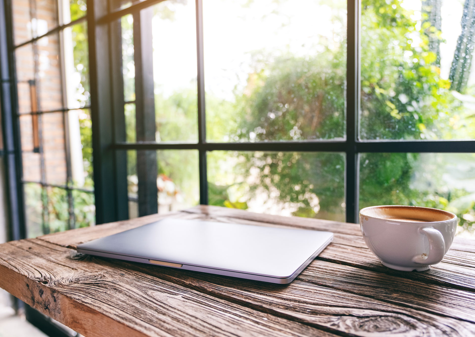 Kaffee und Laptop stehen auf dem Tisch vor dem Fenster